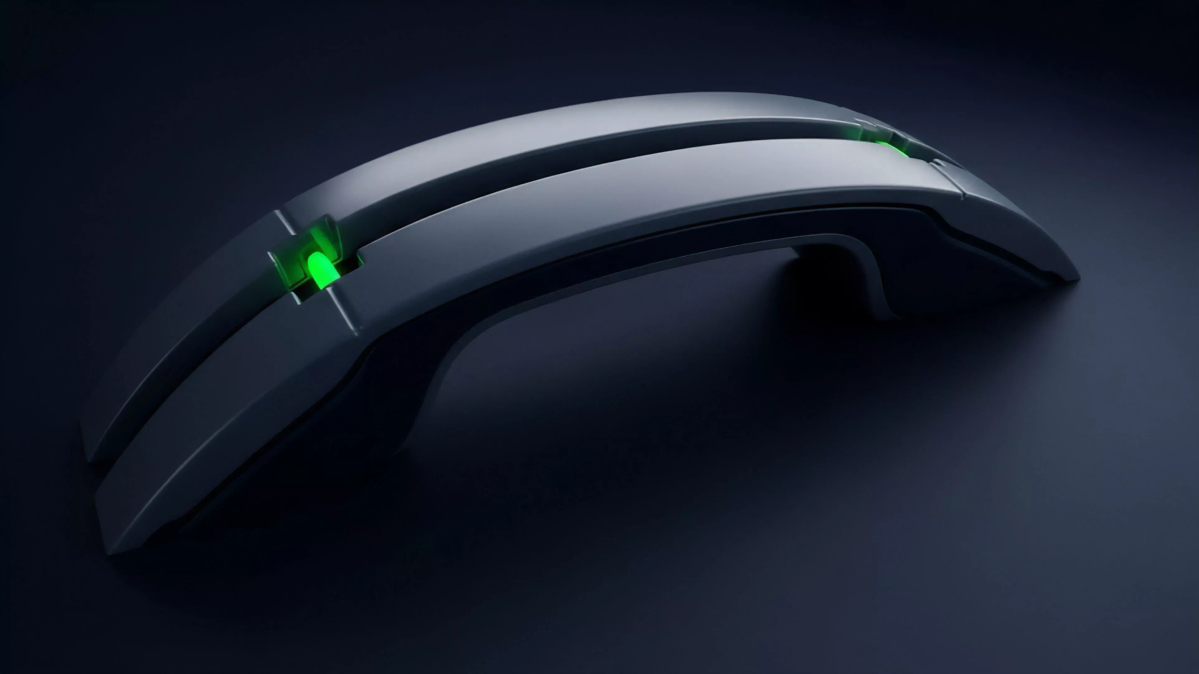 A sleek, curved electronic device with a metallic finish is depicted against a dark background. A bright green light shines from a central groove on its top surface, highlighting the high-tech design and reflective contours