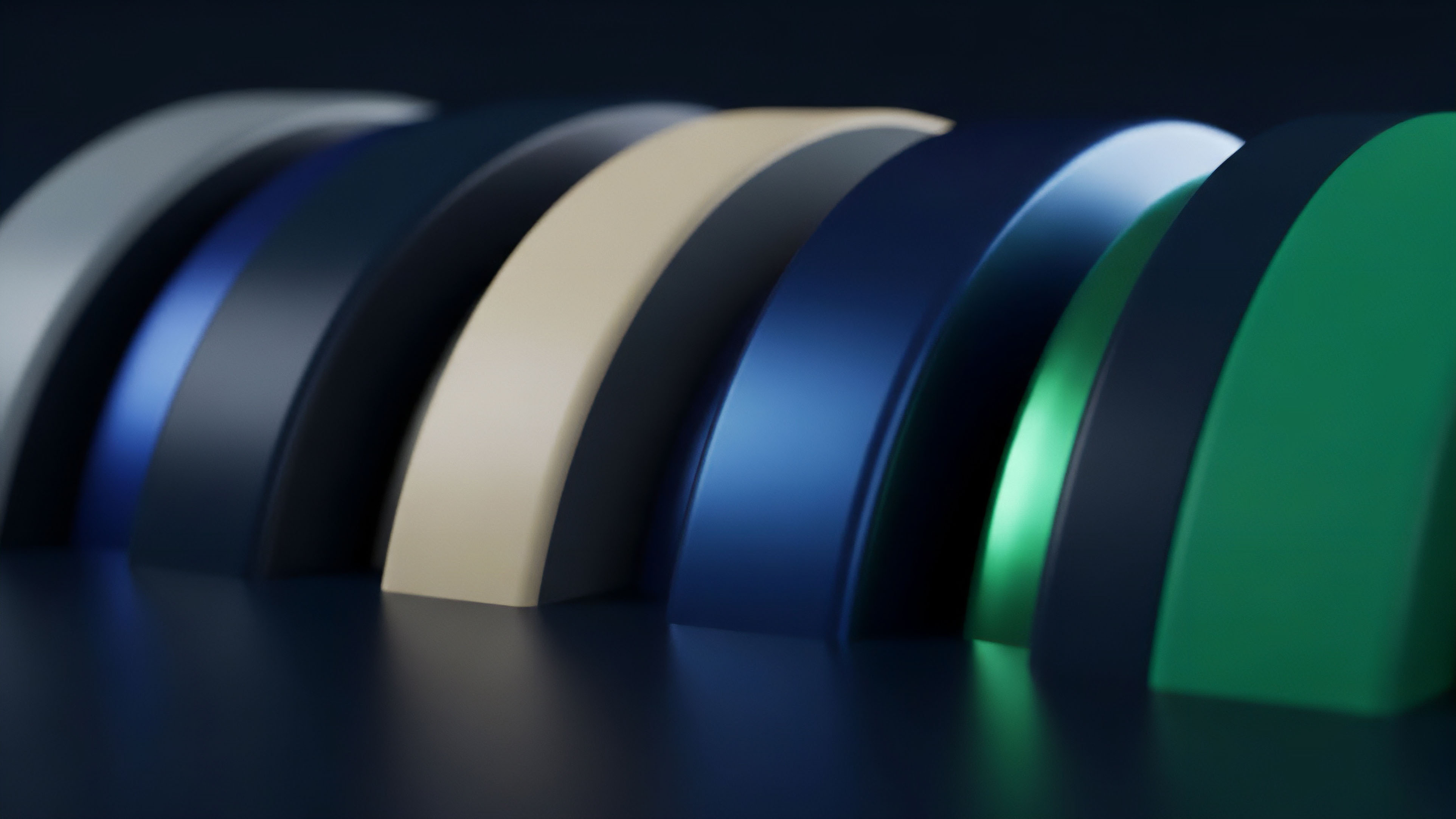 A row of layered, curved shapes in various colors, ranging from cool blues and greens to a warm beige, rests on a reflective dark surface. The shapes transition in color and texture, some appearing matte while others have a metallic sheen