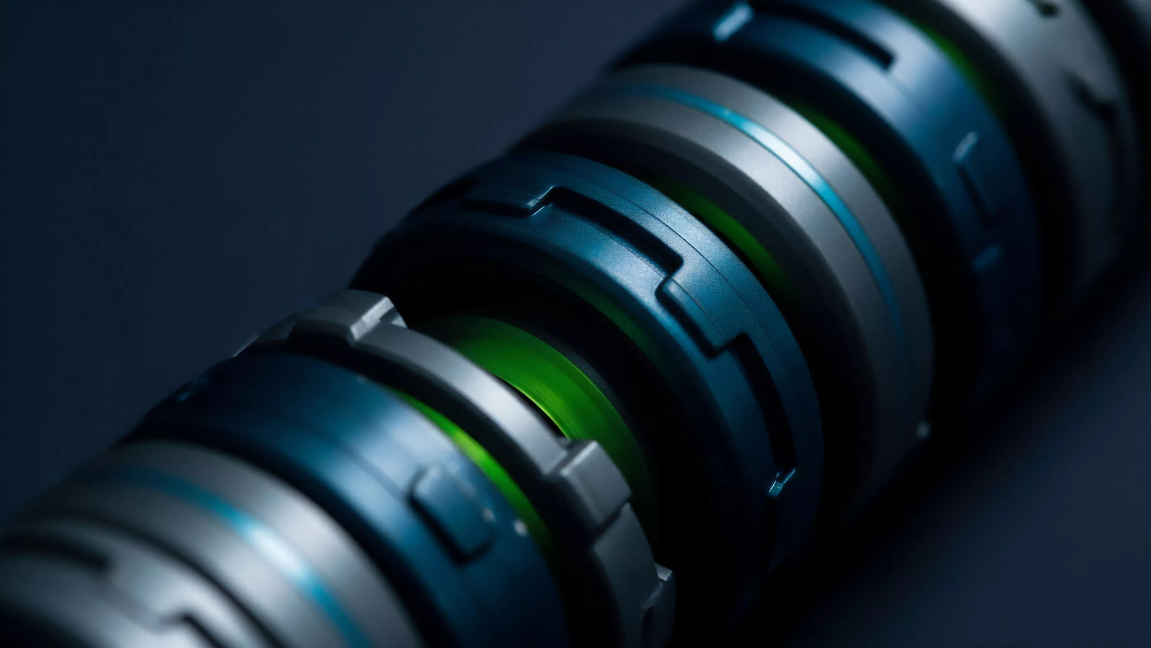 A high-resolution macro shot captures the intricate details of a futuristic cylindrical object, featuring interlocking segments of varying textures and colors. The focal point is a vibrant green glowing ring, flanked by dark blue and metallic gray components